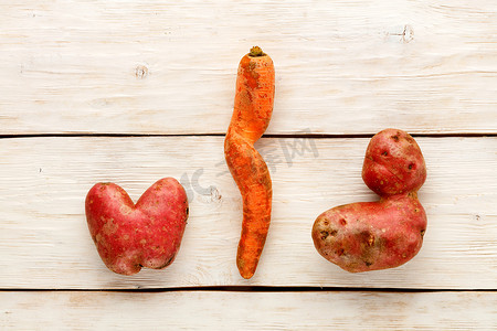 心形丑陋的土豆和白色木制背景上扭曲的胡萝卜。