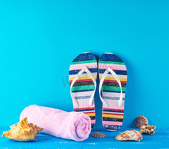 沙滩拖鞋摄影照片_一双女式沙滩拖鞋和蓝色背景上的粉色毛巾