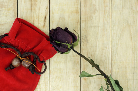 木纹背景上带红色小袋子的干玫瑰
