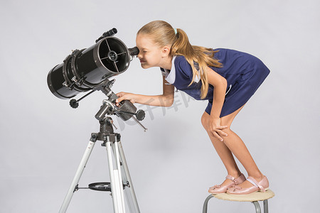 七岁女孩站在椅子上，在望远镜反射镜的目镜中看起来很可笑