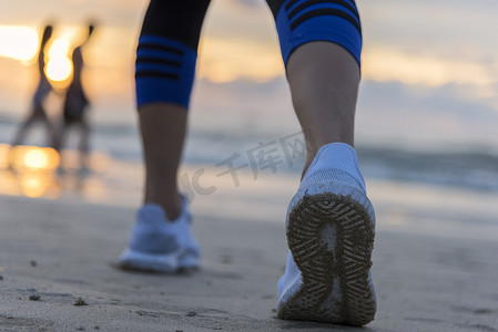 女人在日出时在沙滩上跑步，特写是鞋子。