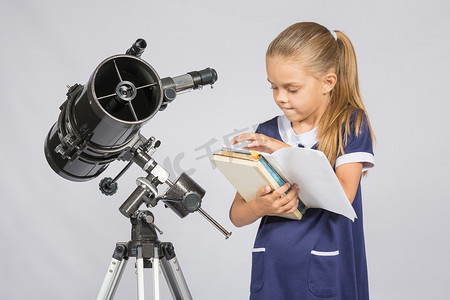学生望远镜摄影照片_女学生天文学家翻阅书籍，在望远镜台上找到正确的信息