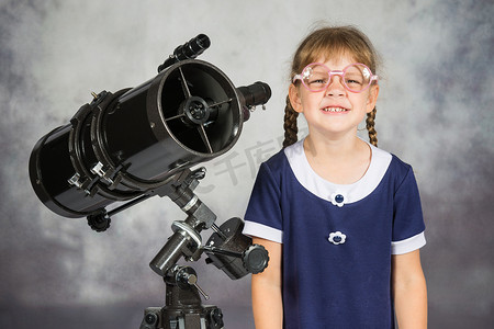 学生望远镜摄影照片_戴着眼镜的业余天文学家滑稽地微笑着站在望远镜旁