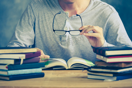 关闭一个男人拿着眼镜，在木桌上看书。