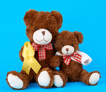 棕色泰迪熊坐着，爪子上拿着一条黄色丝带