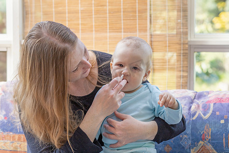婴儿护理的母亲给她的孩子喷鼻剂治疗感冒