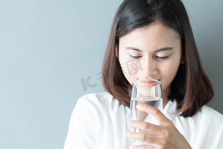 特写女人从玻璃杯中喝纯净水，玻璃中有光
