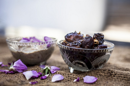 在透明玻璃碗中特写流行的印度和亚洲冬季甜点，即 Khajor ka halwa 或日期甜点，在棕色表面上带有生日期和一些玫瑰花瓣。