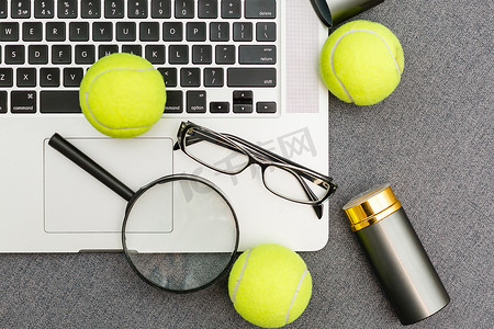 电脑器材摄影照片_笔记本电脑、运动器材、网球、羽毛球、体育管理灰色桌子上的眼镜的顶视图。经营理念。