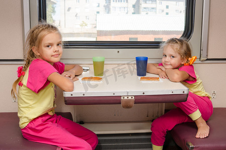 二等奖等奖摄影照片_火车上的两个小女孩穿着同样的衣服坐在外二等车厢的桌子旁