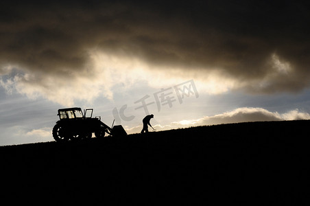 棉塞摄影照片_农夫在他的拖拉机旁边工作的剪影高在云端