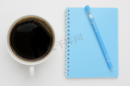 vi工作摄影照片_咖啡杯和蓝色笔记本，白色背景笔，顶部 vi
