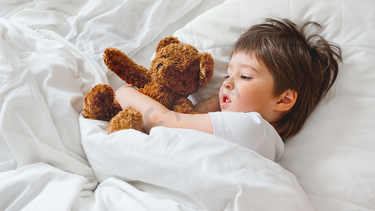 躺在床上摄影照片_蹒跚学步的孩子和可爱的泰迪熊躺在床上。