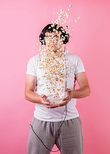 年轻有趣的男人把爆米花扔到空中，与粉红色隔离