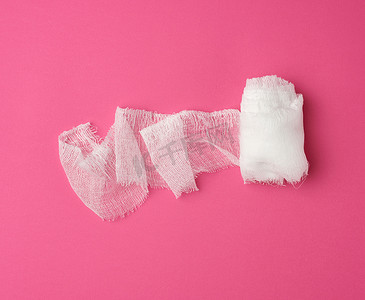 纱布白色摄影照片_粉红色背景中的一卷白色纱布绷带