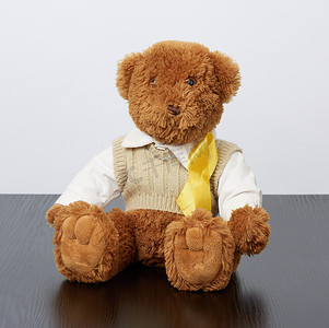 棕色泰迪熊坐着，一条黄色丝带放在黑色木头上