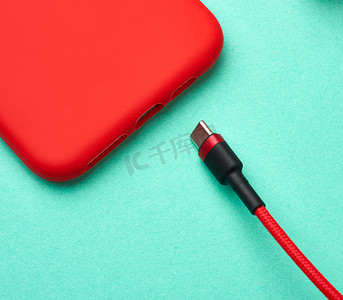 绿色背景中纺织编织物中的红色智能手机和电缆