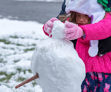 雪地里玩耍摄影照片_在前花园的雪地里玩耍的蹒跚学步的女孩