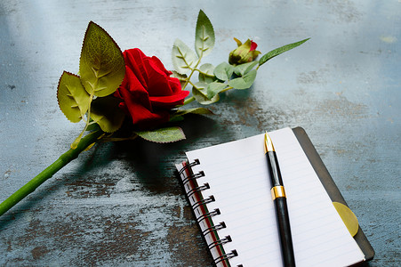空白页笔记本、笔和一朵美丽的红玫瑰在质朴的金属地板背景上，带有复制空间。