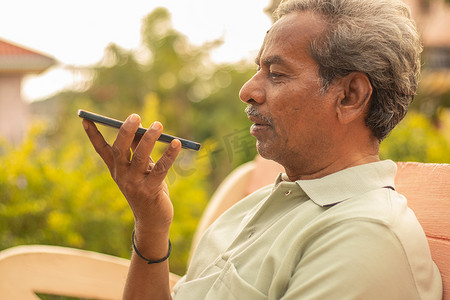 在电话中使用虚拟助手的老人-印度老人在手机上使用语音命令-老人在户外用智能手机交谈。