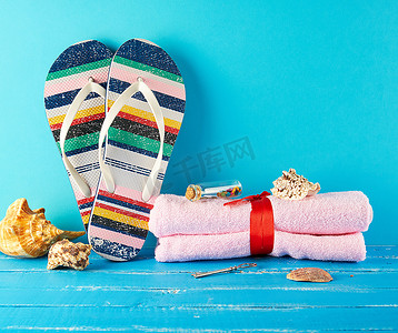 一双女式沙滩拖鞋和蓝色背景上的粉色毛巾