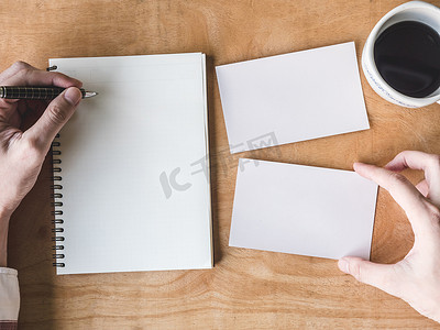 男性手在木桌上用空白照片卡和咖啡杯在笔记本上写一些数据的顶视图。