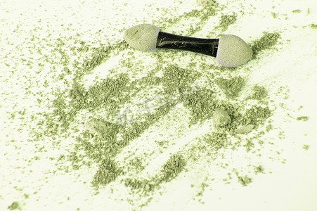 散落的橄榄色和绿色眼影，带有涂抹器，以白色背景、美容和化妆概念为背景