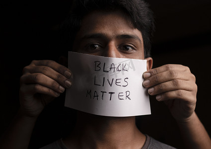 lives摄影照片_年轻人的脸上贴着 Black Lives Matter 纸质海报-对黑人的种族歧视概念。