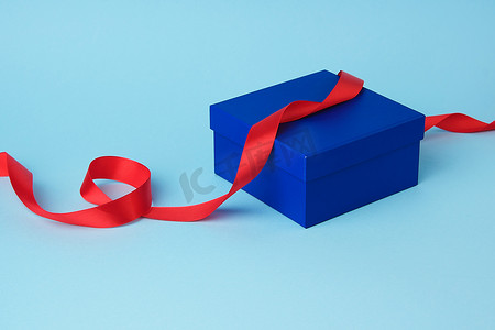 礼物的方形的蓝色纸板箱和被扭曲的丝绸红色丝带
