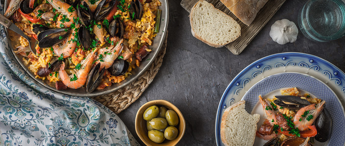深色石桌上的西班牙海鲜饭盘子，配以不同的配饰宽屏