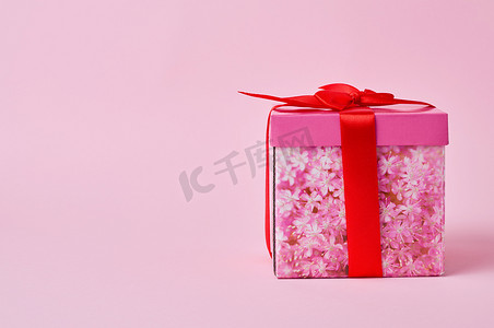 盒子粉色摄影照片_方形纸板粉色盒子，在粉色背景上系着红色蝴蝶结