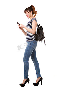 女孩拿包摄影照片_白色背景下拿着手机和包走路的年轻女子的侧面肖像