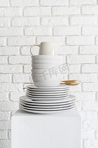 白色砖墙背景上的一堆白色陶瓷盘子和餐具