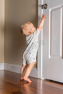 拉小手摄影照片_刚能走路的小婴儿伸手去拿木地板上的门把手