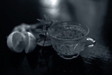 在木质表面的透明杯子中关闭由威士忌、生姜、蜂蜜、水、柠檬和薄荷组成的草药绿茶。