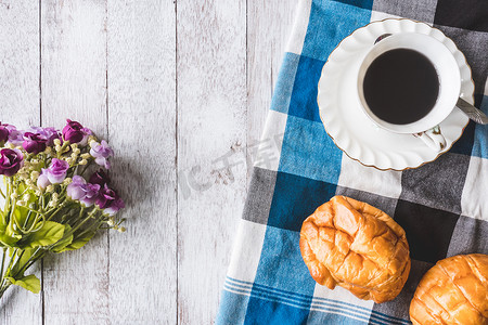 木桌背景上带面包、鲜花和桌布的咖啡杯的顶部视图