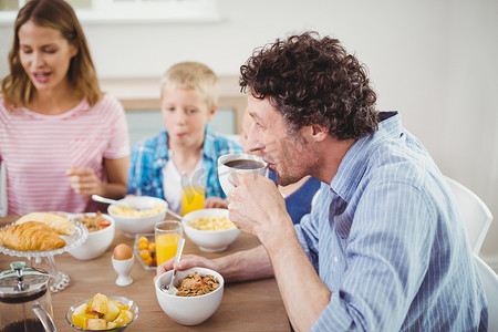 母亲喝茶摄影照片_男人在与家人共进早餐时喝茶