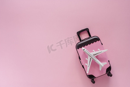 小飞机旅游摄影照片_白色飞机模型，粉红色背景中带小行李