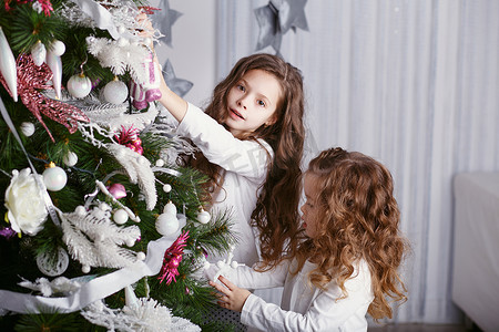两个小姐妹用玩具和球装饰圣诞树