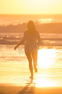 海滩奔跑的美摄影照片_夕阳下在沙滩上奔跑的女人。