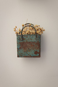 一束细小的人造花，干草色，放在一个蓝色的金属盒子里，非常古老且生锈，挂在墙上