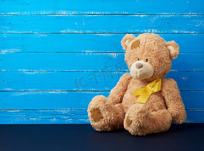 黄色丝带摄影照片_棕色泰迪熊坐着，一条黄色丝带放在蓝色木头上