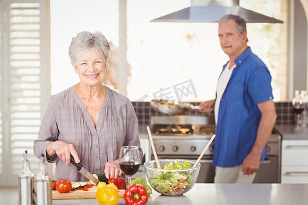 背景中与丈夫一起切菜的快乐老年妇女