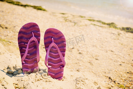 沙滩拖鞋摄影照片_沙滩上的紫色沙滩拖鞋
