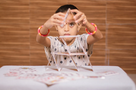 在家里忙着用纸牌屋建造金字塔的小女孩 — 学童专注或专注运动游戏的概念