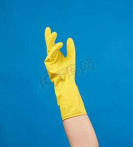 一只女性手上穿着用于清洁的黄色橡胶手套，蓝色