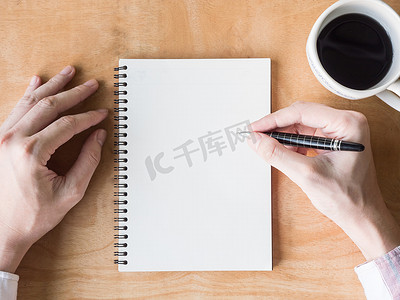 男性手在笔记本上写一些数据的顶部视图，木桌上的咖啡杯
