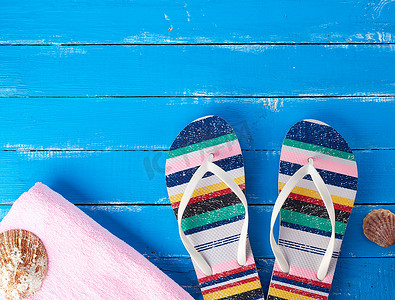 一双女式沙滩拖鞋和蓝色背景上的粉色毛巾
