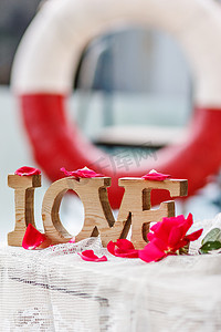 玫瑰艺术字摄影照片_背景粉红色玫瑰花瓣中的木雕“爱”字