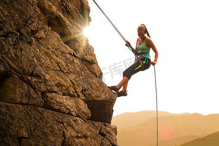美丽的女人在山上雾蒙蒙的日落时爬上岩石。